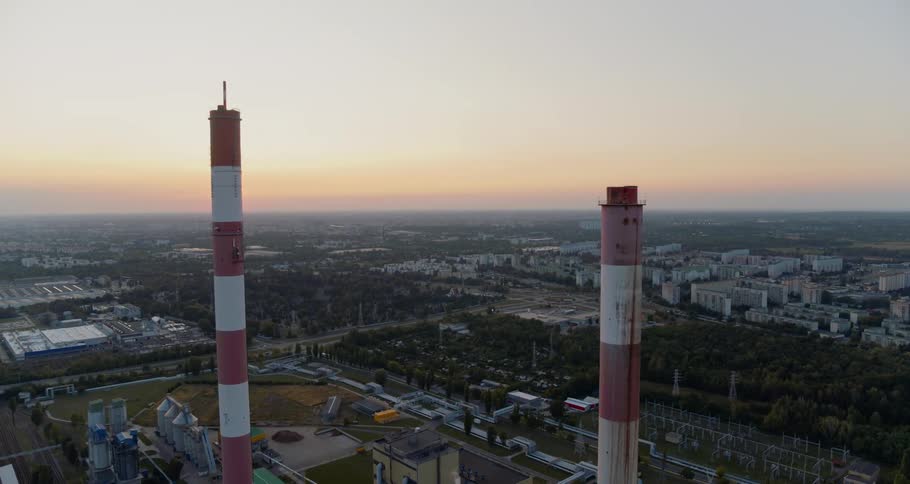 A large industrial facility with two tower smokestacks is surrounded by a large number of other buildings