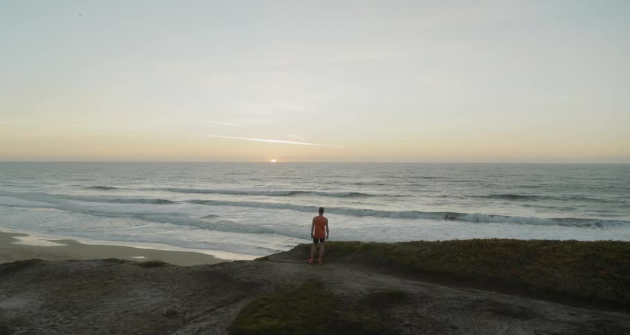 A man watches the sunset on top of a cliff by the ocean