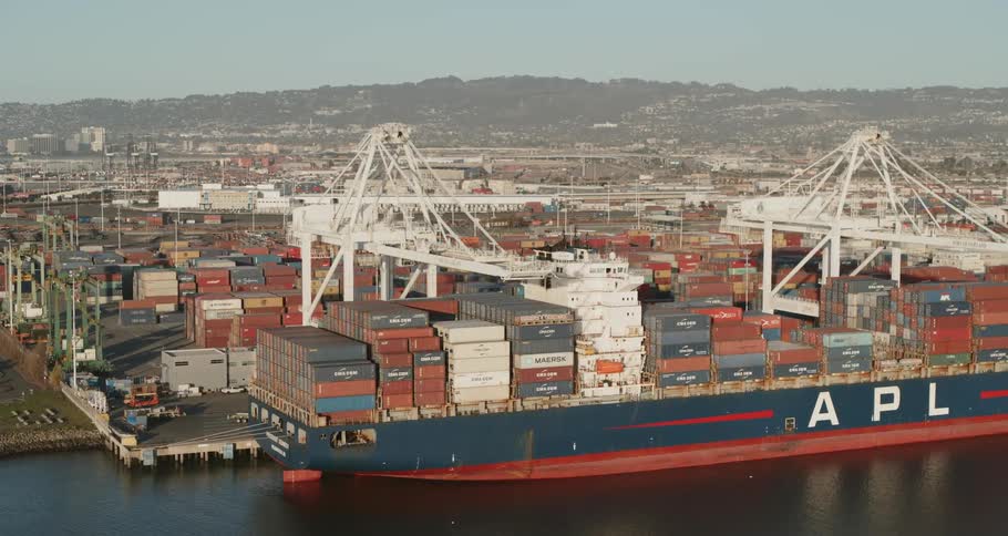 Cranes stand over a barge loaded with shipping containers on the waterfront