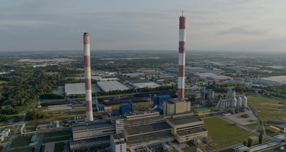 A large factory has two towering smokestacks painted with red and white stripes