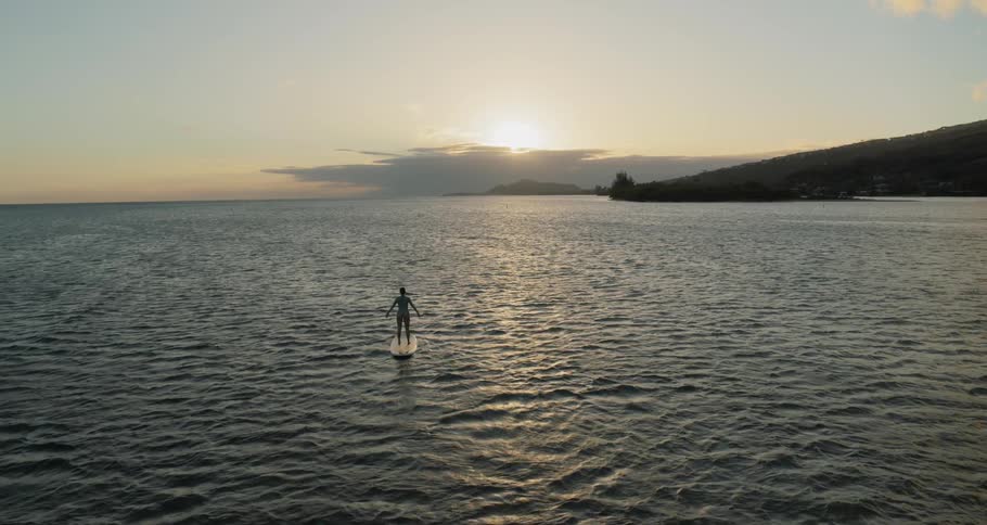 A woman standing on a surfboard and lifting her arms while on the ocean