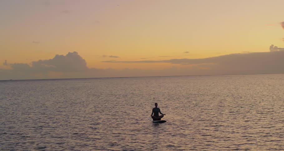 Woman does a yoga pose while sitting on a surfboard in the ocean