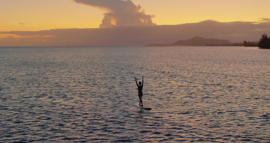 A woman does yoga standing on a surfboard