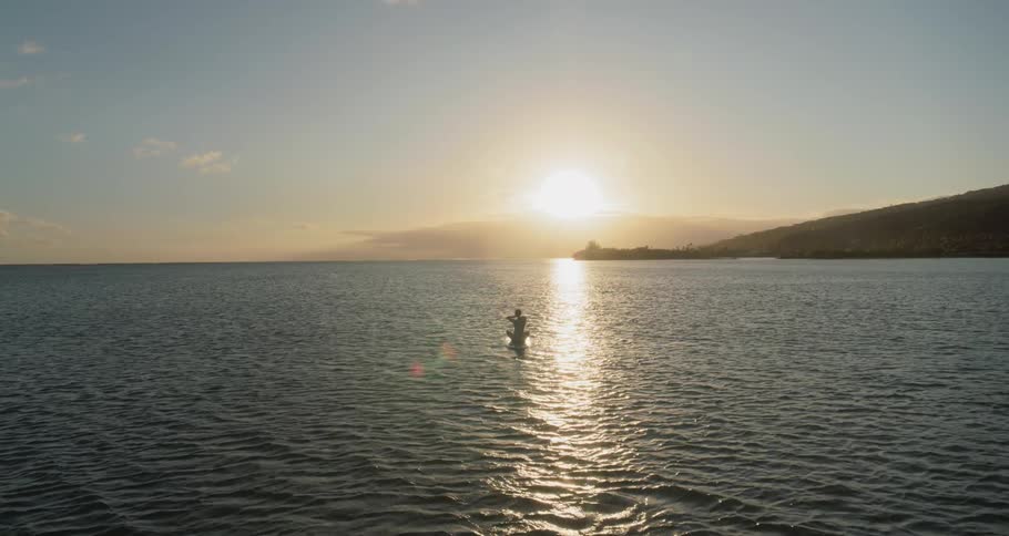 A woman sits on a surfboard in the ocean at sunset