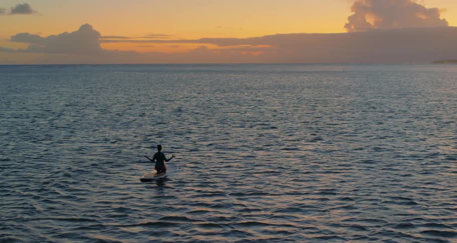 A woman meditates on a paddle board in the ocean