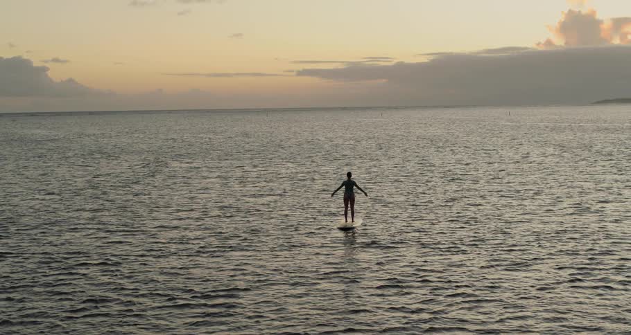 A woman does yoga on a surfboard in the middle of the ocean