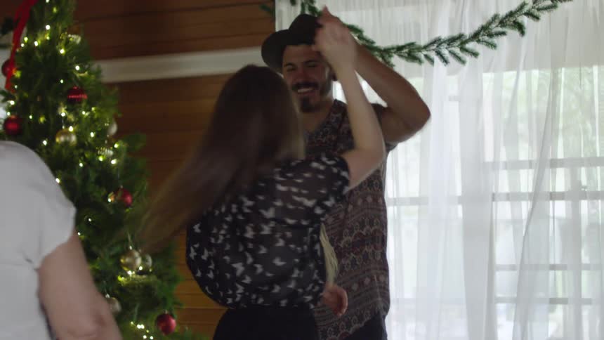 A young woman twirls in front of her partner at a family christmas gathering inside their home