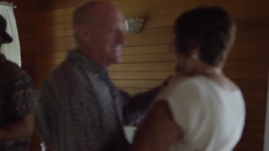 Couples dancing in front of a fireplace in a room with paneled walls and large windows