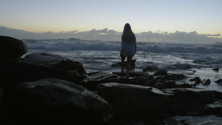 A woman walking a rocky shore at sunset