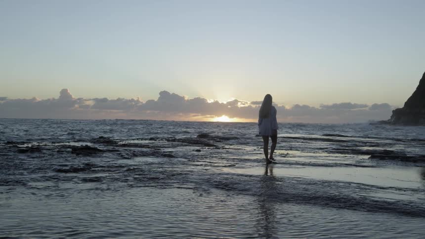 A woman walks the shore at sunrise