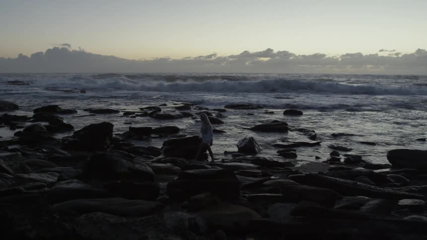 A woman walking along a rocky shore at sunrise