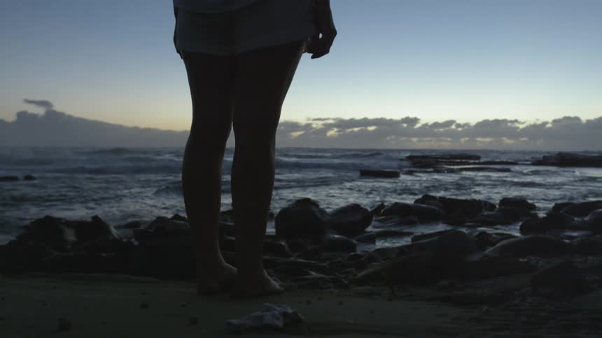 Woman standing on a rocky beach at dusk