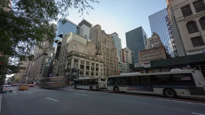 Pedestrians walk in the city as buses taxis and cars travel on a busy city street