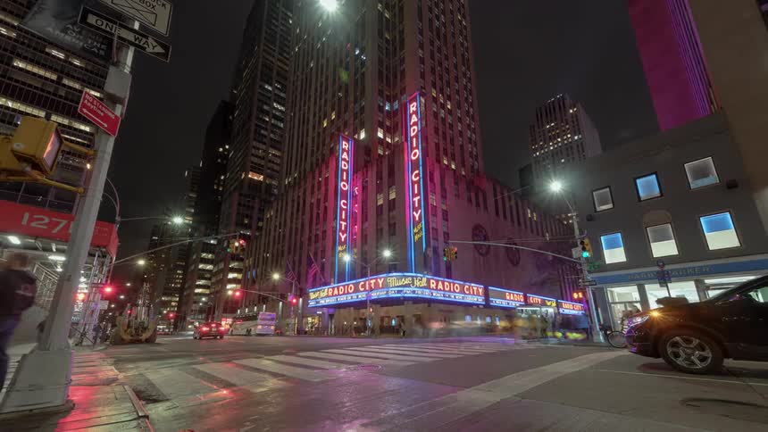 People and traffic move around radio city music hall in rockefeller center at night