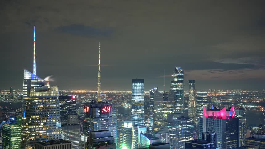 The colorful spires and glowing hm sign of the new york city skyline at night
