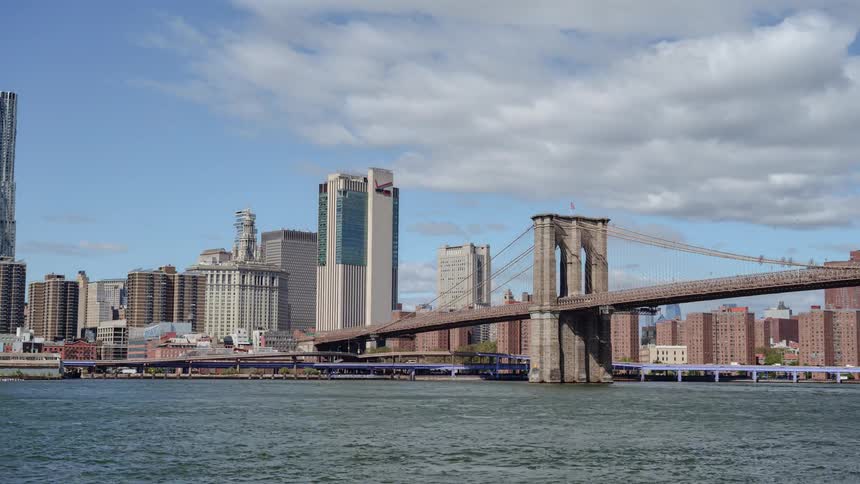 Boats go down a river under a bridge near a large city