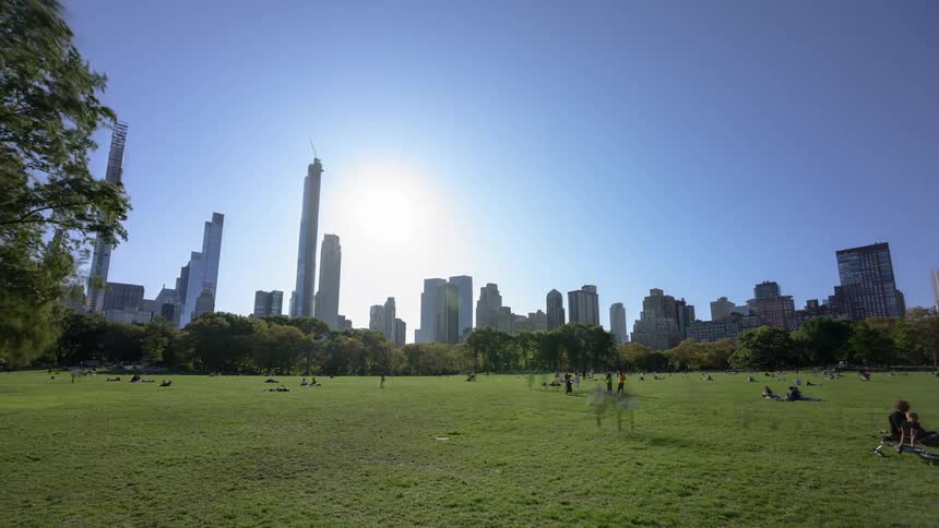 People picnic and relax on the green grass of the park with the city skyline behind