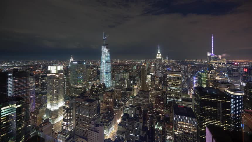 Clouds move through night sky over brightly lit city downtown