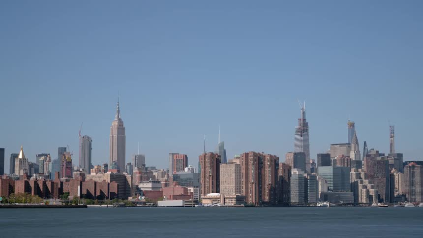 Boats pass through water in front of city downtown under clear blue sky