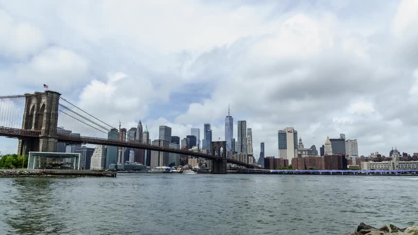 Boats travel under the brooklyn bridge with the manhattan skyline on the horizon