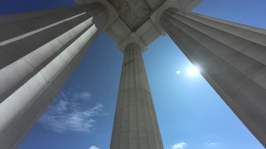 Sunlight shines down on tall stone building pillars