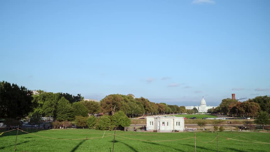 Traffic passes along road through large lawns with capitol building on horizon