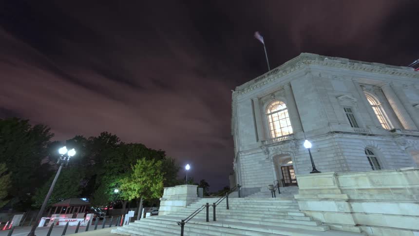 Flag flaps on top of government buildingas clouds pass over head at night