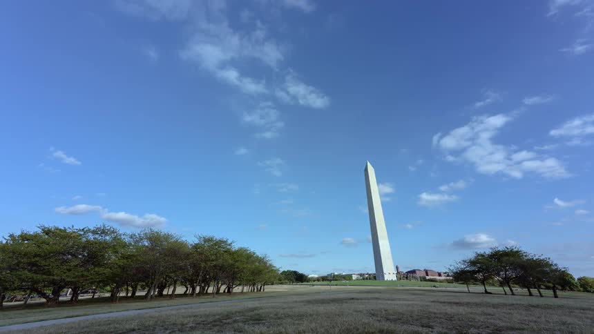 Tall monument sits under a blue sky as pedestrians walk by