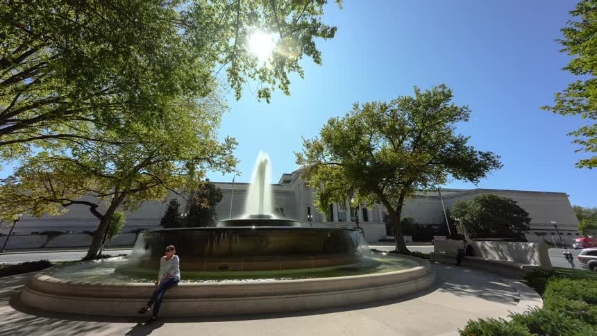 A water fountain flows in the center of a town square with tourists coming and going
