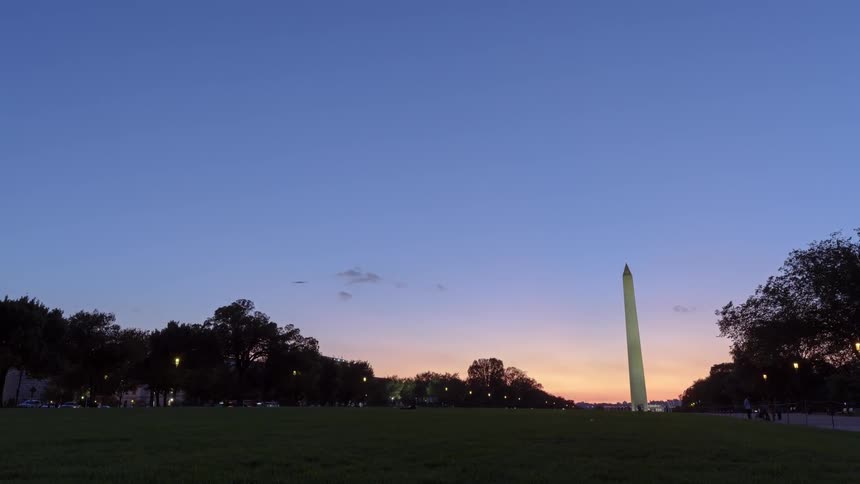 A tall column like monument in a field between two roads