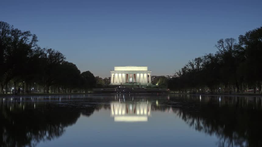 People walk around a reflection pool near a memorial