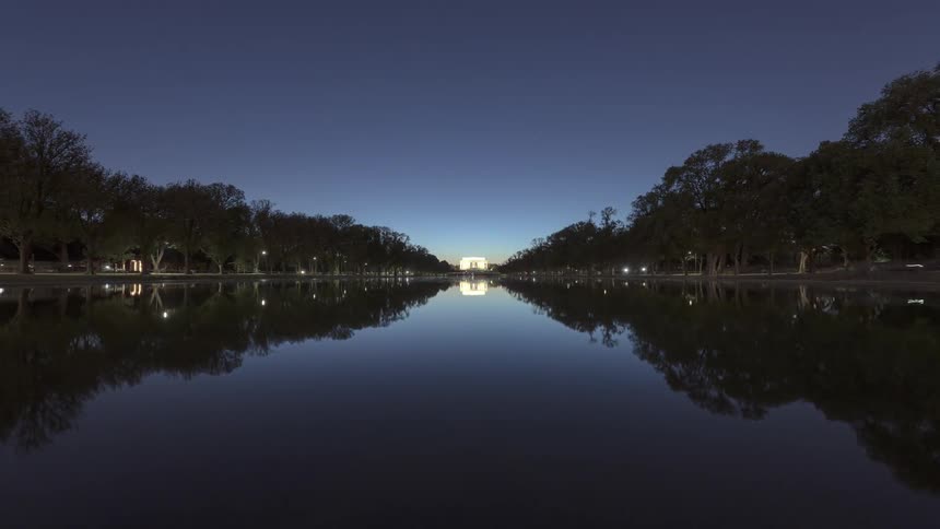 Traffic passes on either side of wide tree lined lake
