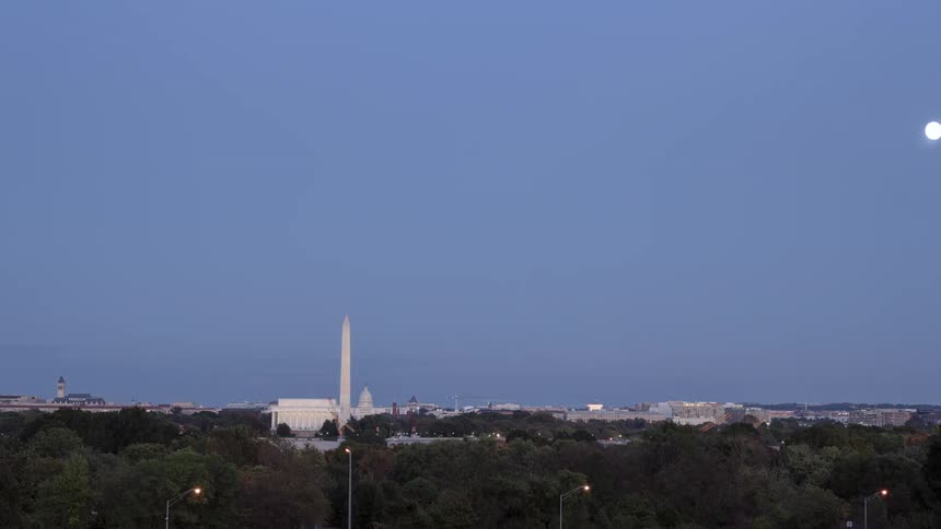 The moon rises over the city as darkness falls