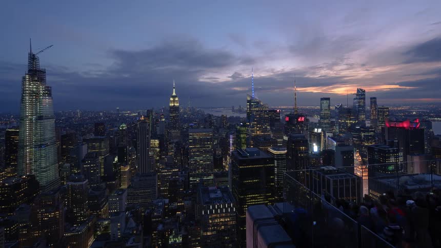 Scores of people crowd an observation deck to take pictures of a city skyline
