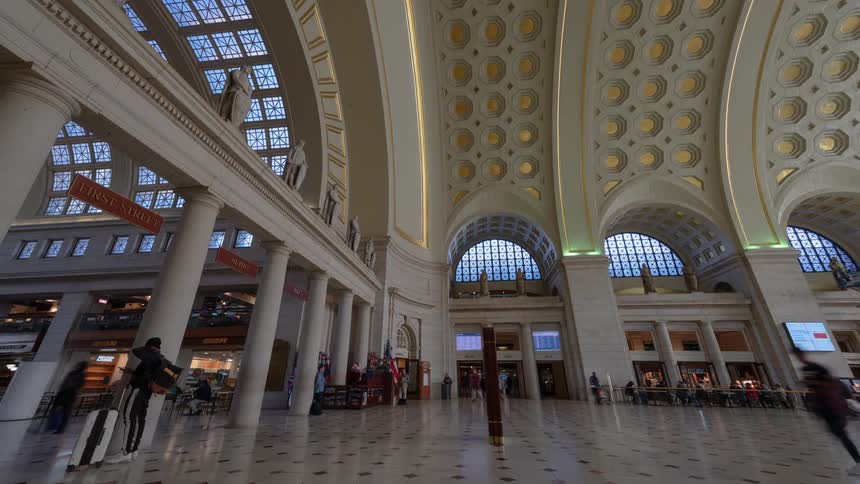 Pedestrians walk through building lobby with high arched ceiling lights