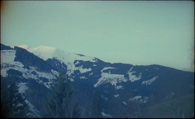 Snow capped mountains and trees seen from a deck where an ashtray sits on the railing