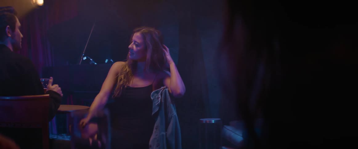 A woman runs her hand through her hair while sitting in a dark bar