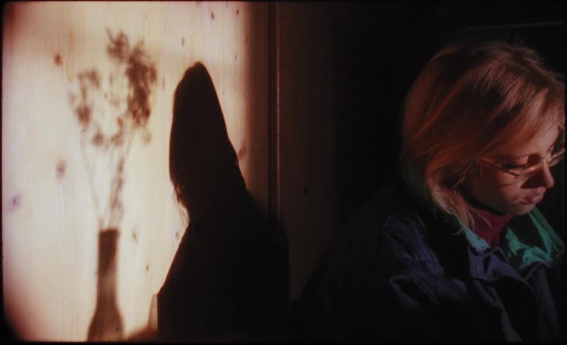 A woman sits in front of a wall with a shadow of a vase and flowers