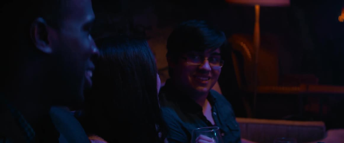 A woman holding a wine glass and sitting between two others turns her head and talks while all three smile
