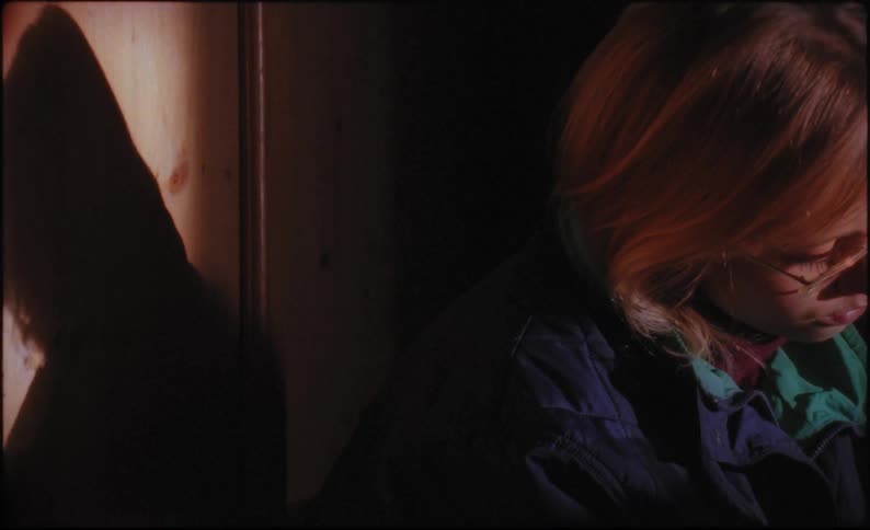 A person in a jacket sitting in a dark room adjusting their eyeglasses