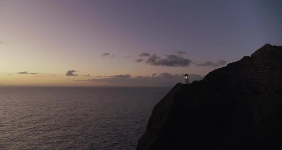 A lighthouse shines on a mountain top beside the ocean