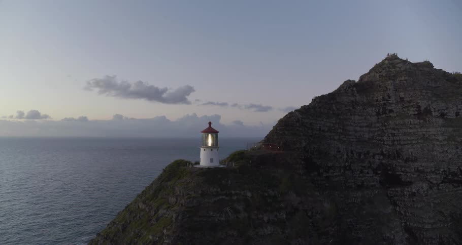 Lighthouse beacon twirls on promontory overlooking ocean