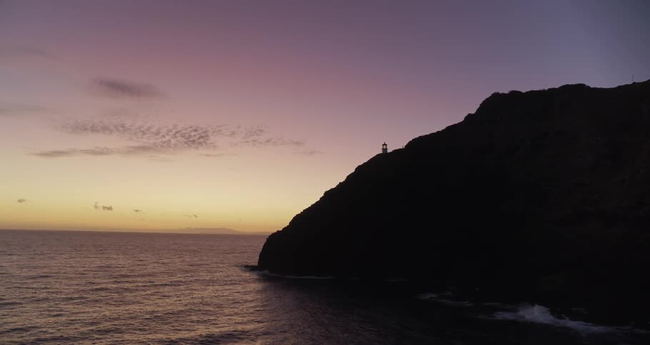 A lighthouse on an ocean cliff during sunset