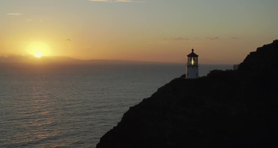 A lighthouse on a cliff bordering the ocean at sunset