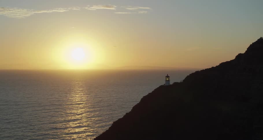 The sun setting over the water and a light house on a hill