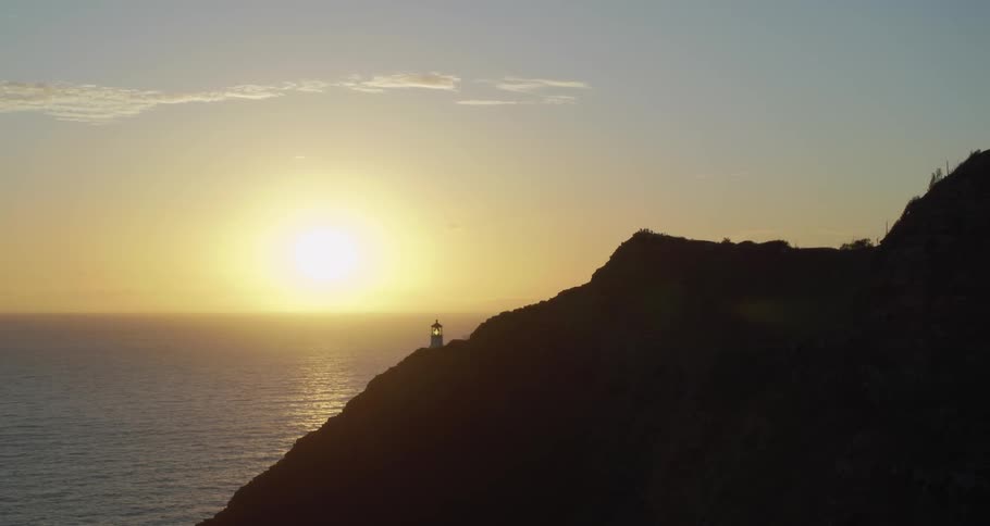 A lighthouse sits on a mountainside beside the ocean