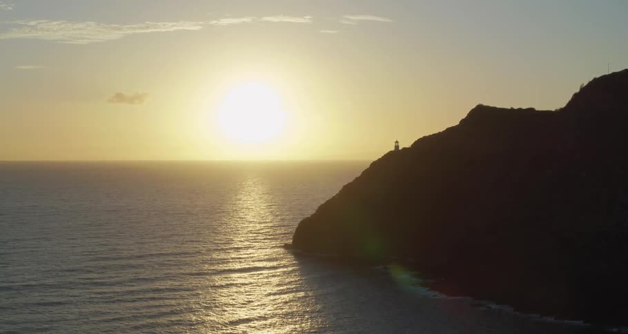 Sun rises on horizon near lighthouse on promontory