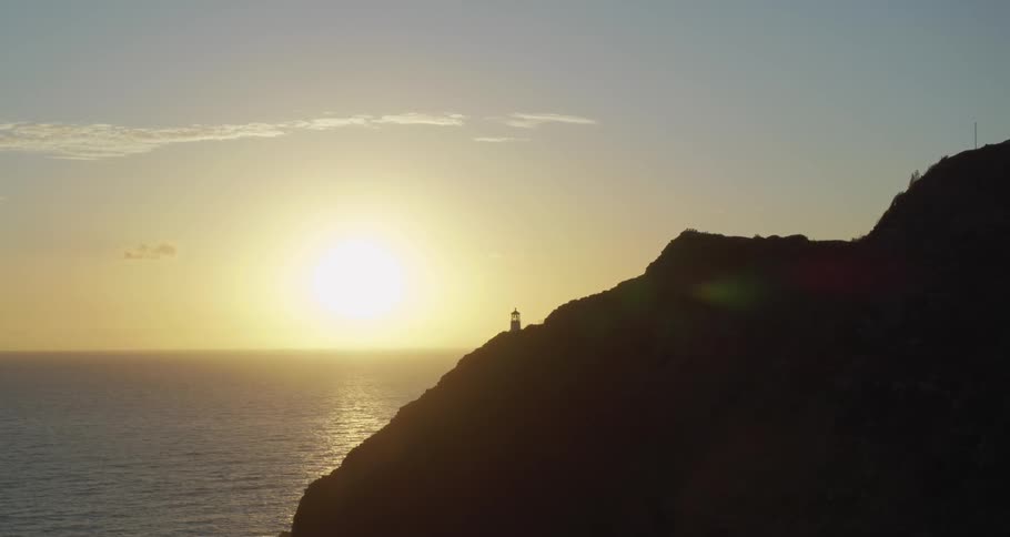 Lighthouse sits on promontory overlooking ocean as sun rises on the horizon