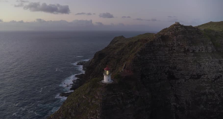 A light glows and shines in a lighthouse on a cliff ridge above the ocean