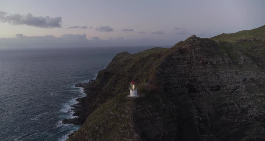 A lighthouse beach glows on an oceanside cliff at dusk